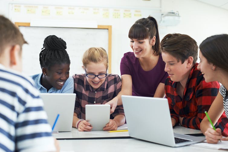 Enseignant et adolescents utilisant des tablettes et des ordinateurs portables.